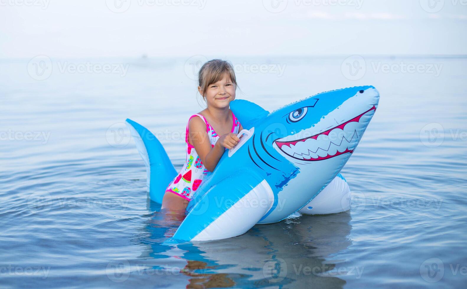 content fille de européen apparence âge de sept nager sur un gonflable gros requin jouet dans le mer.famille été vocation concept. photo