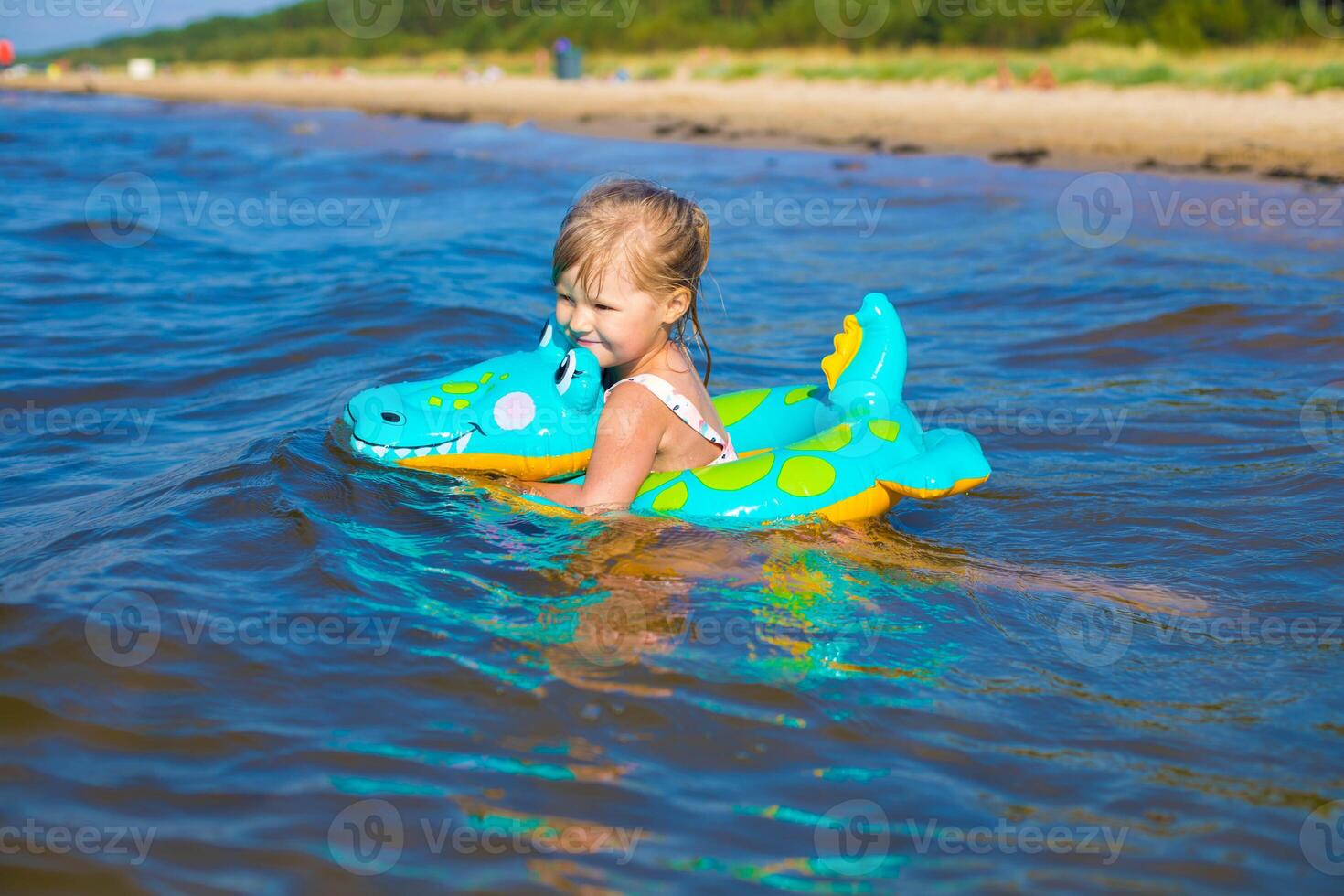 content fille de européen apparence âge de 5 nager sur un gonflable crocodile jouet dans le mer.enfants apprendre à nager.peu bébé fille avec gonflable jouet flotte en jouant dans l'eau sur été vocation.famille été vocation concept. photo