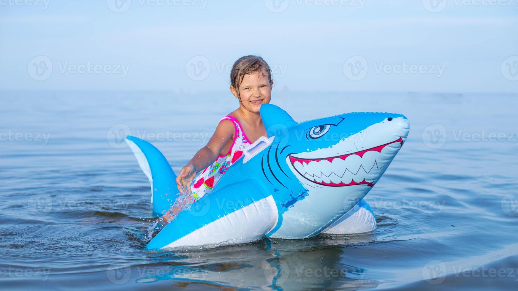 content fille de européen apparence âge de sept nager sur un gonflable gros requin jouet dans le mer.famille été vocation concept. photo