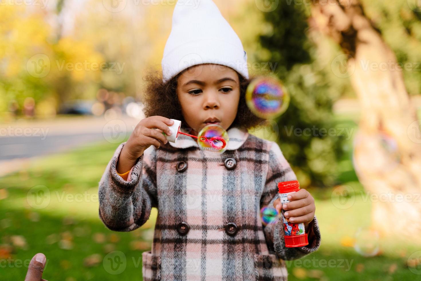 fille noire soufflant des bulles de savon pendant la marche dans le parc d'automne photo
