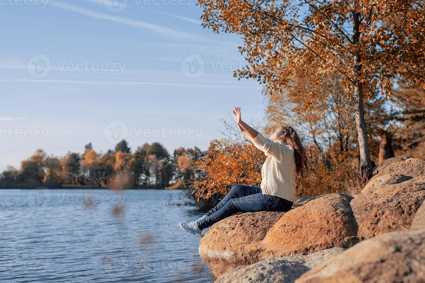 femme romantique réfléchie assise sur des rochers au bord de la rivière au coucher du soleil en journée d'automne photo