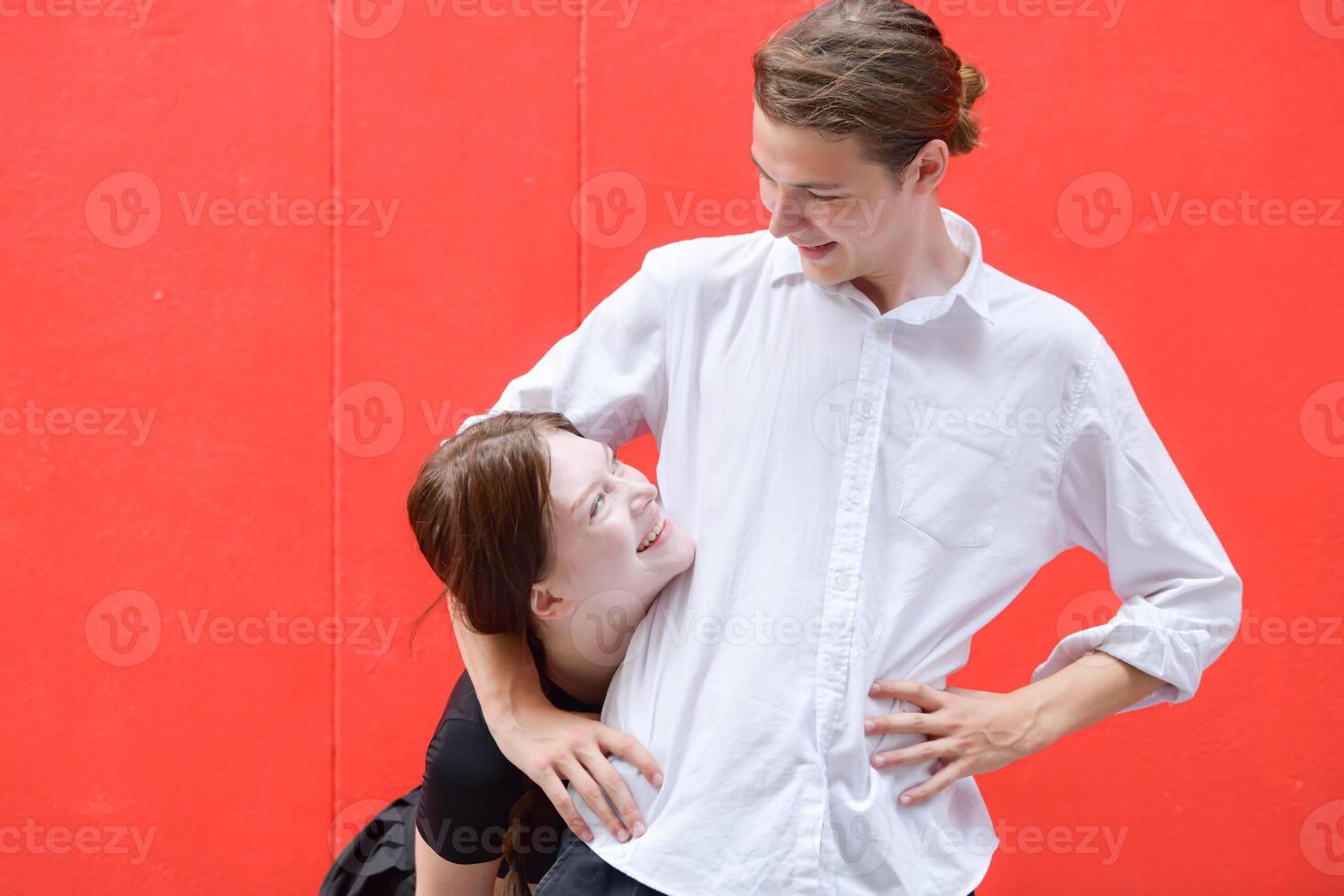 une couple est profiter une été vacances dans le rouge mur arrière-plan, Heureusement montrant leur l'amour à chaque autre. photo