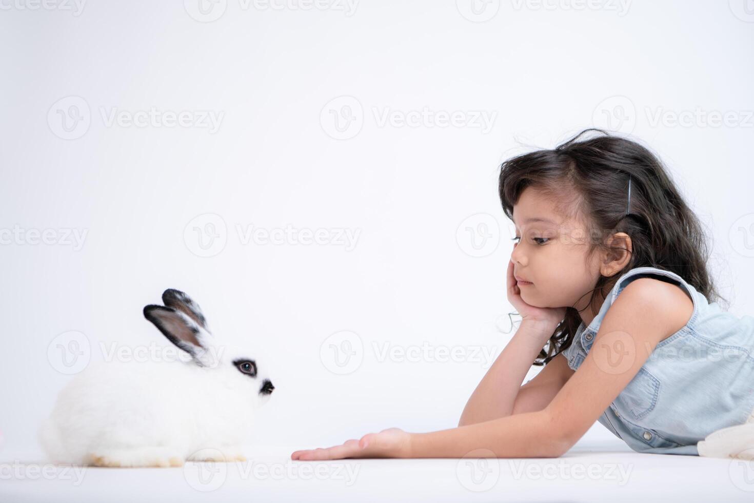 souriant peu fille et avec leur bien-aimée duveteux lapin, mettant en valeur le beauté de relation amicale entre humains et animaux photo