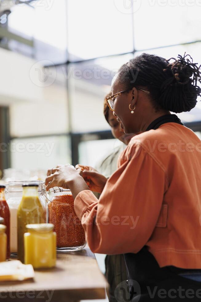 africain américain vendeur dans une magasin, des offres Conseil et sert sa les clients avec fraîchement récolté, biologique bio aliments. côté vue de sa interaction avec un la personne dans éco amical local supermarché. photo