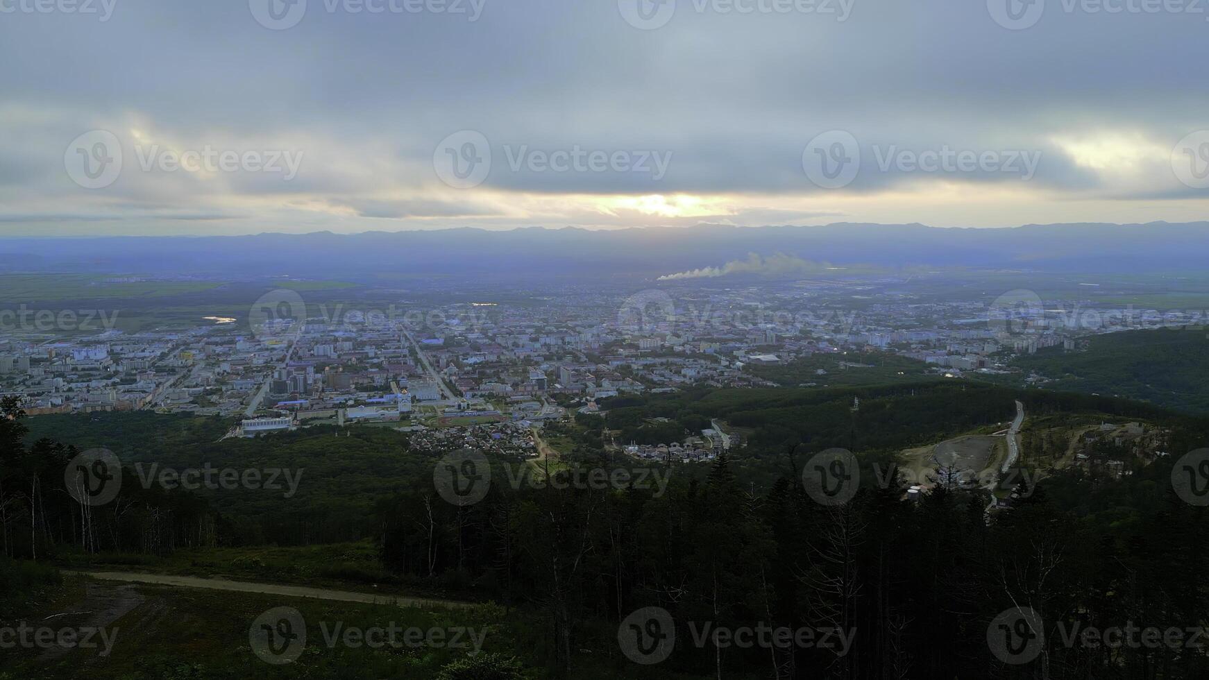 aérien vol une descente le vert montagnes vers touristique ville. agrafe. été vert des arbres sur une colline pente et le ville avec nuageux ciel au-dessus de. photo