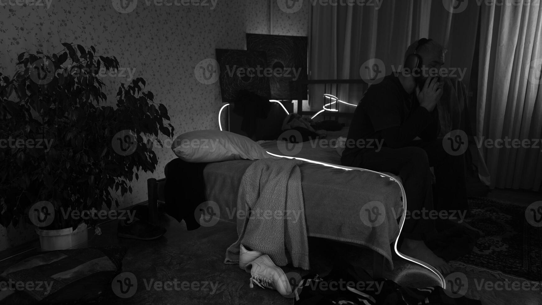 triste homme séance sur lit dans foncé chambre. médias. homme en essayant à traiter avec anxiété par écoute à musique, monochrome. photo