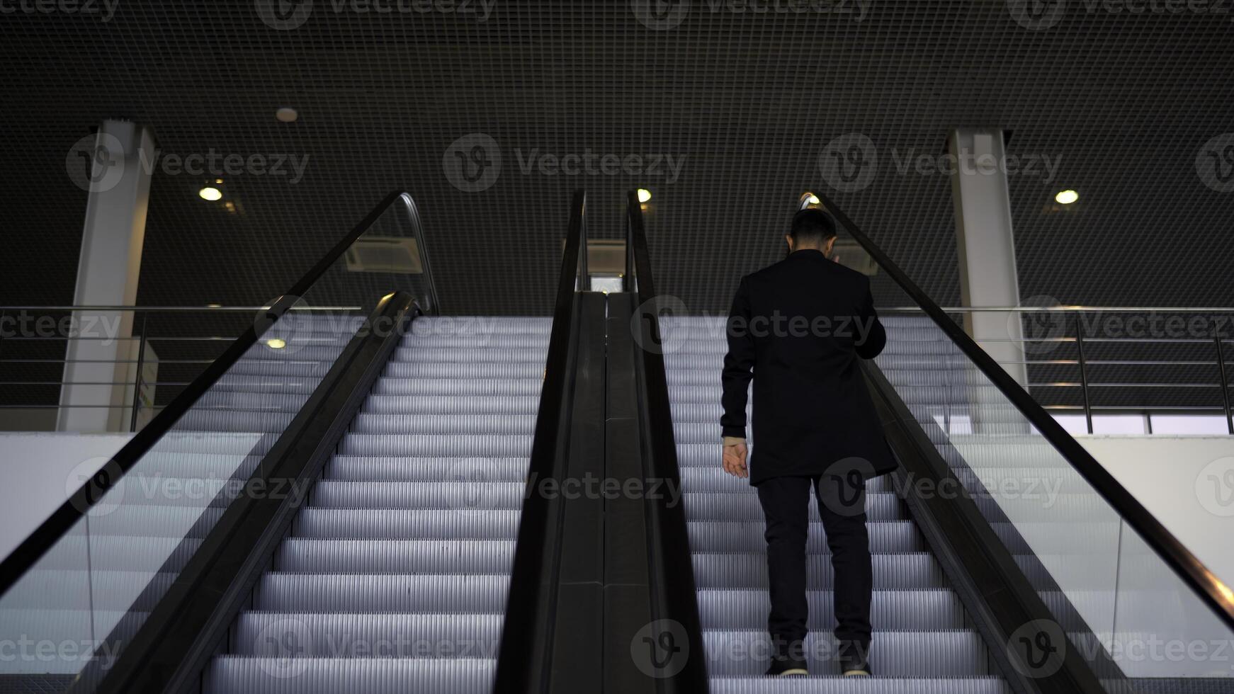 passager équitation sur le escalier mécanique en haut à le station de le sol métro. médias. arrière vue de une Jeune homme d'affaire sur le escalier mécanique. photo