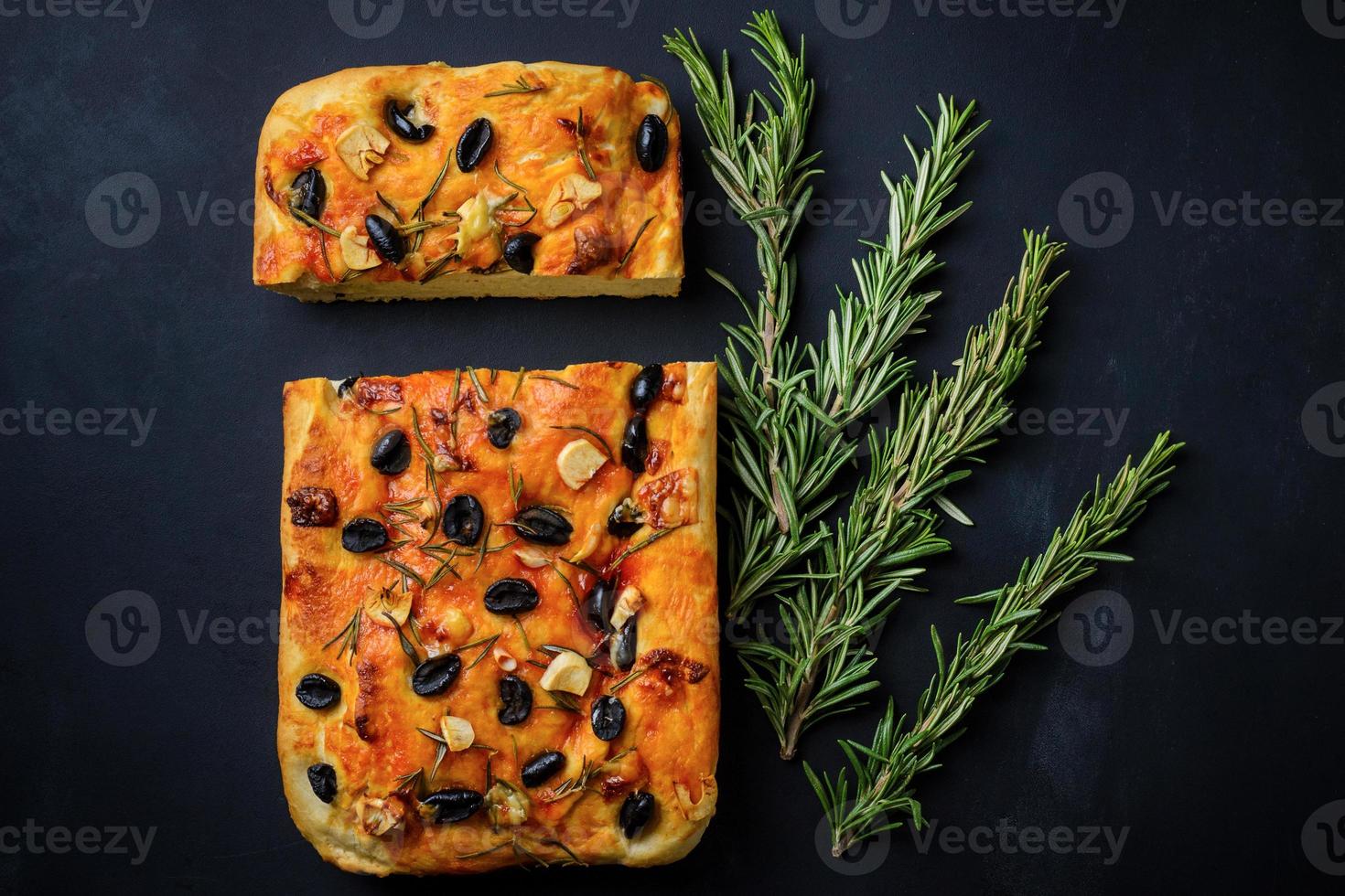 focaccia italienne maison aux olives et romarin et brins de romarin fraîchement sur fond noir photo