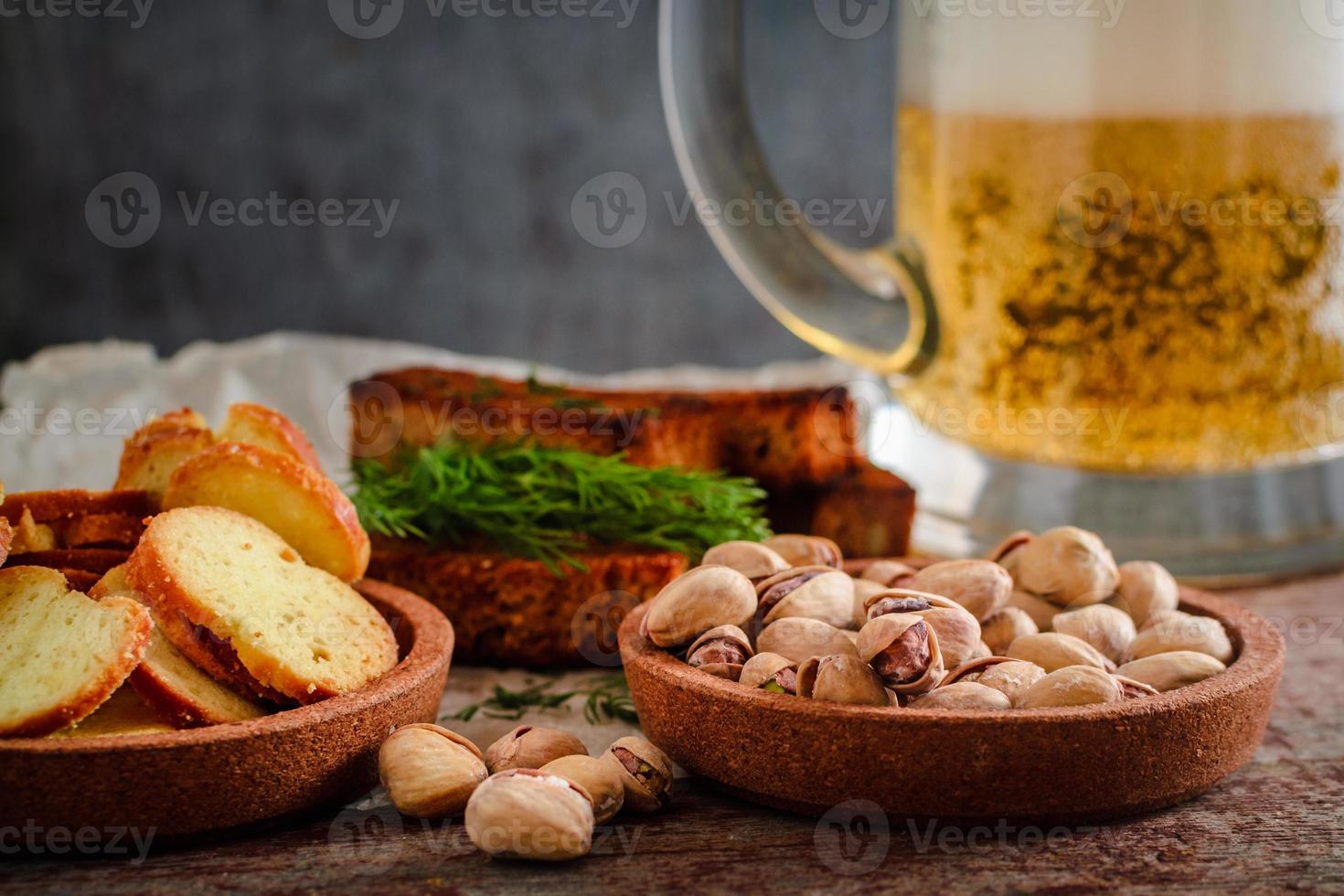 bière dans un verre, pistaches, croûtons de seigle et craquelins sur une table en bois photo