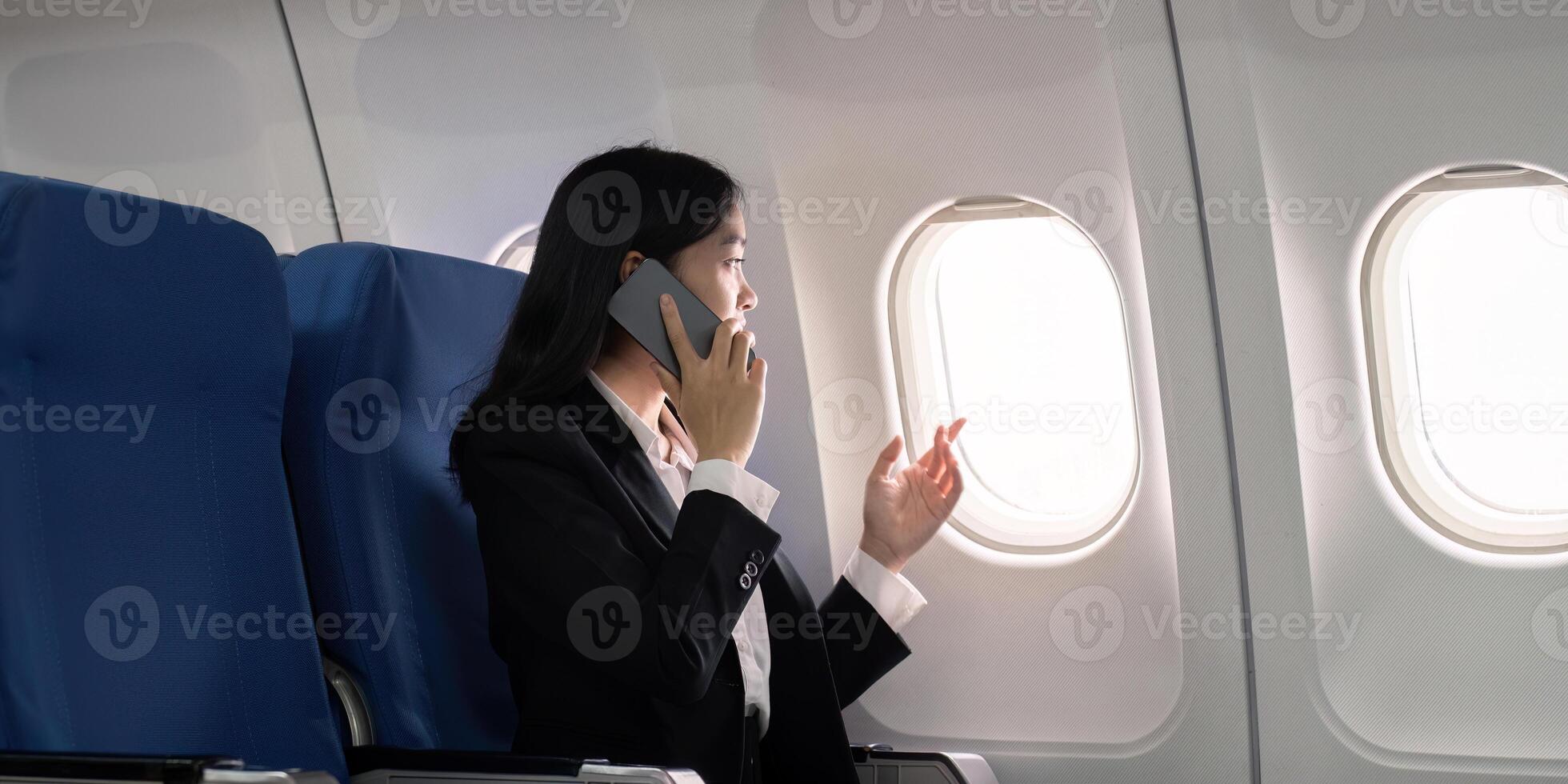 asiatique Jeune femme d'affaires réussi ou femelle entrepreneur dans formel costume dans une avion asseoir dans une affaires classe siège et les usages une téléphone intelligent pendant vol. en voyageant et affaires concept photo