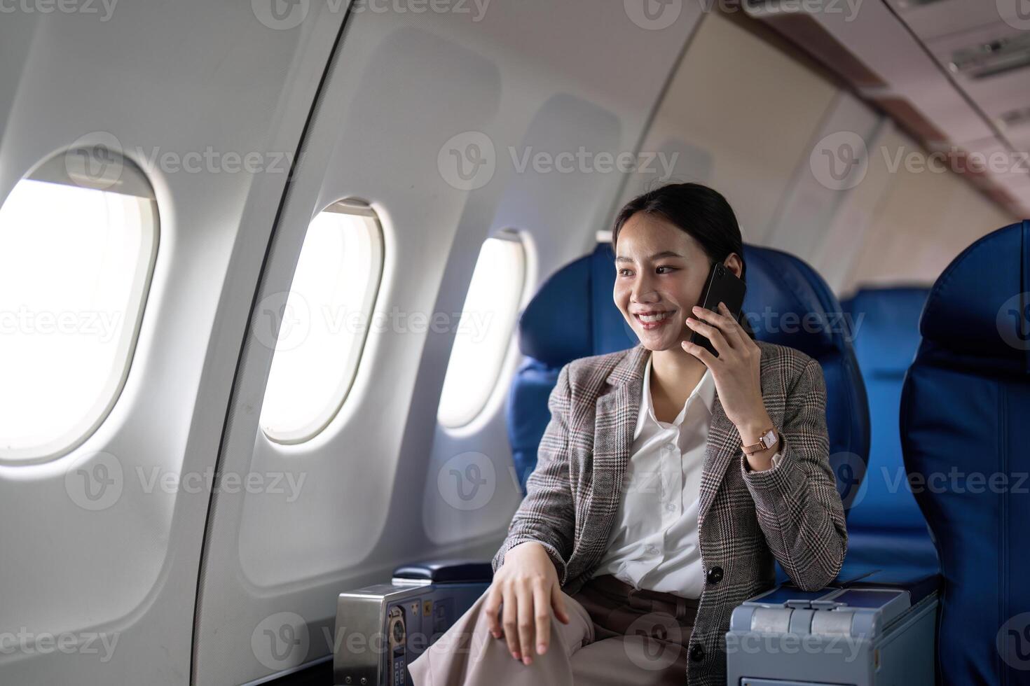 asiatique Jeune femme d'affaires réussi ou femelle entrepreneur dans formel costume dans une avion asseoir dans une affaires classe siège et les usages une téléphone intelligent pendant vol. en voyageant et affaires concept photo