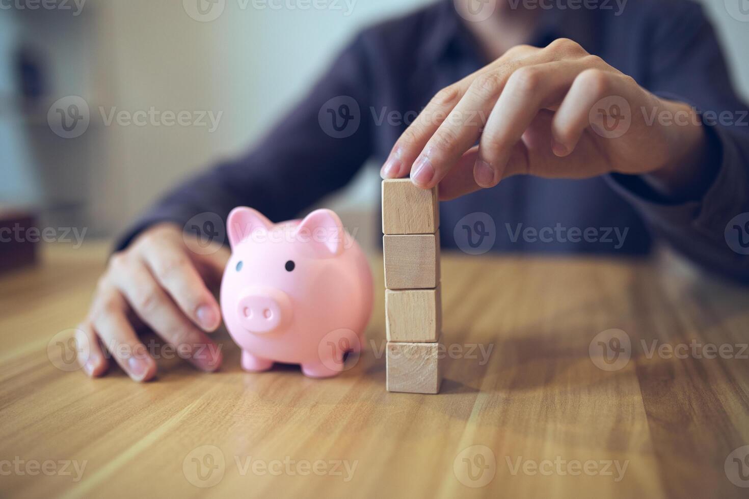 la personne bâtiment une la tour de en bois blocs à côté de une porcin banque, symbolisant financier Planification et économie photo