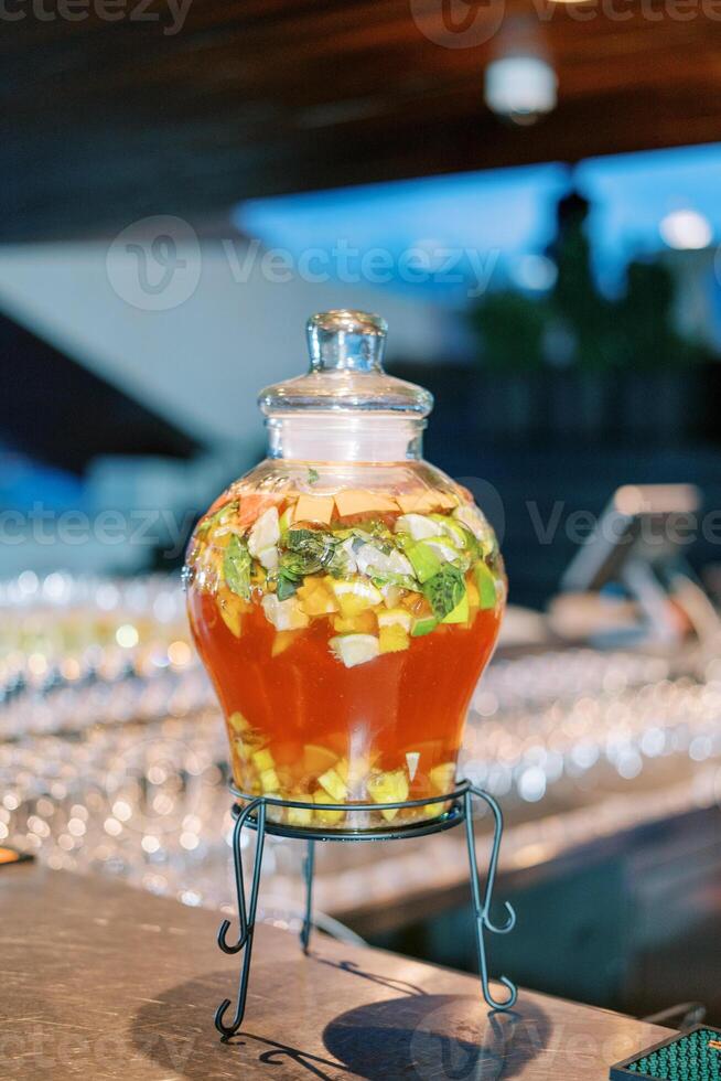 rouge limonade avec pièces de fruit dans une verre pot avec une couvercle sur une supporter des stands sur le table photo