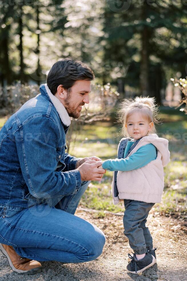 peu souriant fille des stands suivant à squat papa en portant le sien mains dans le parc photo