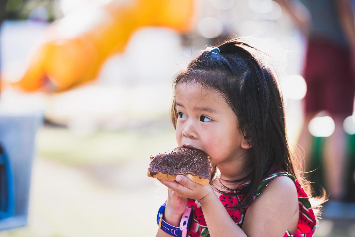 une jolie fille asiatique âgée de 4 à 5 ans mange un délicieux petit pain au chocolat. photo