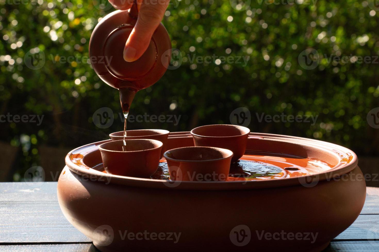 photo de personnes versant du thé chinois d'une petite bouilloire dans une tasse placée sur une table dans un jardin