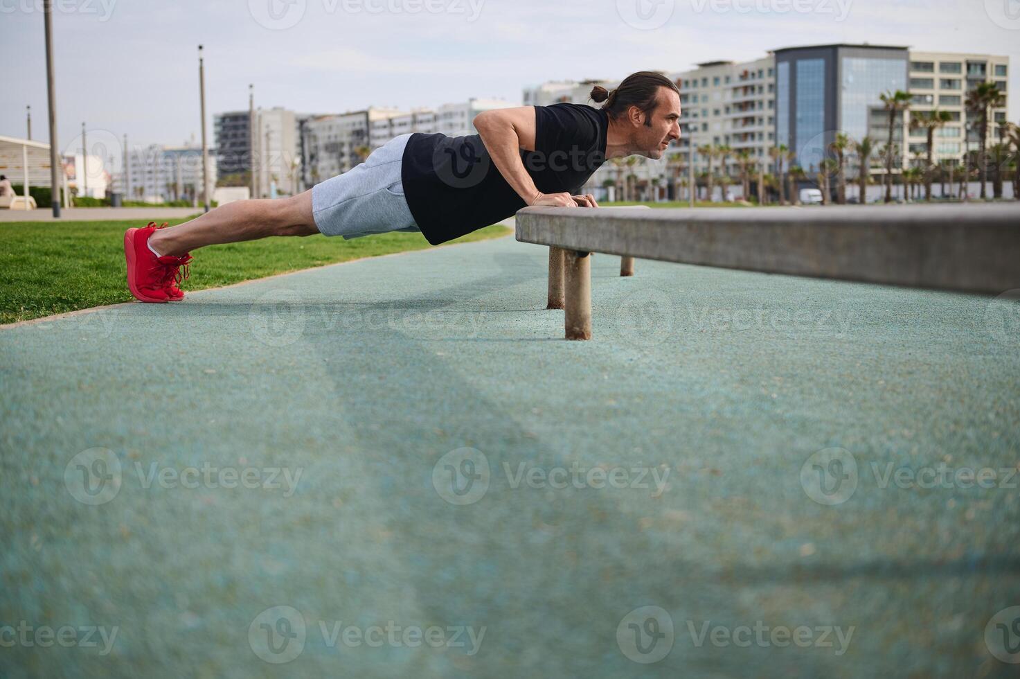caucasien Jeune athlétique homme pompage en haut bras muscles, Faire pousser UPS tandis que travail en dehors en plein air dans Urbain environnement photo