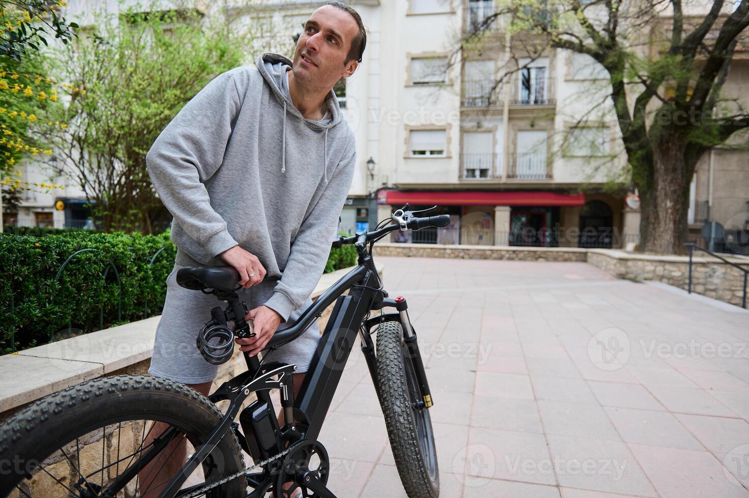 Jeune sportif homme ajuste le la taille de Nouveau batterie alimenté vélo, électrique vélo avant prise il en dehors pour premier balade photo