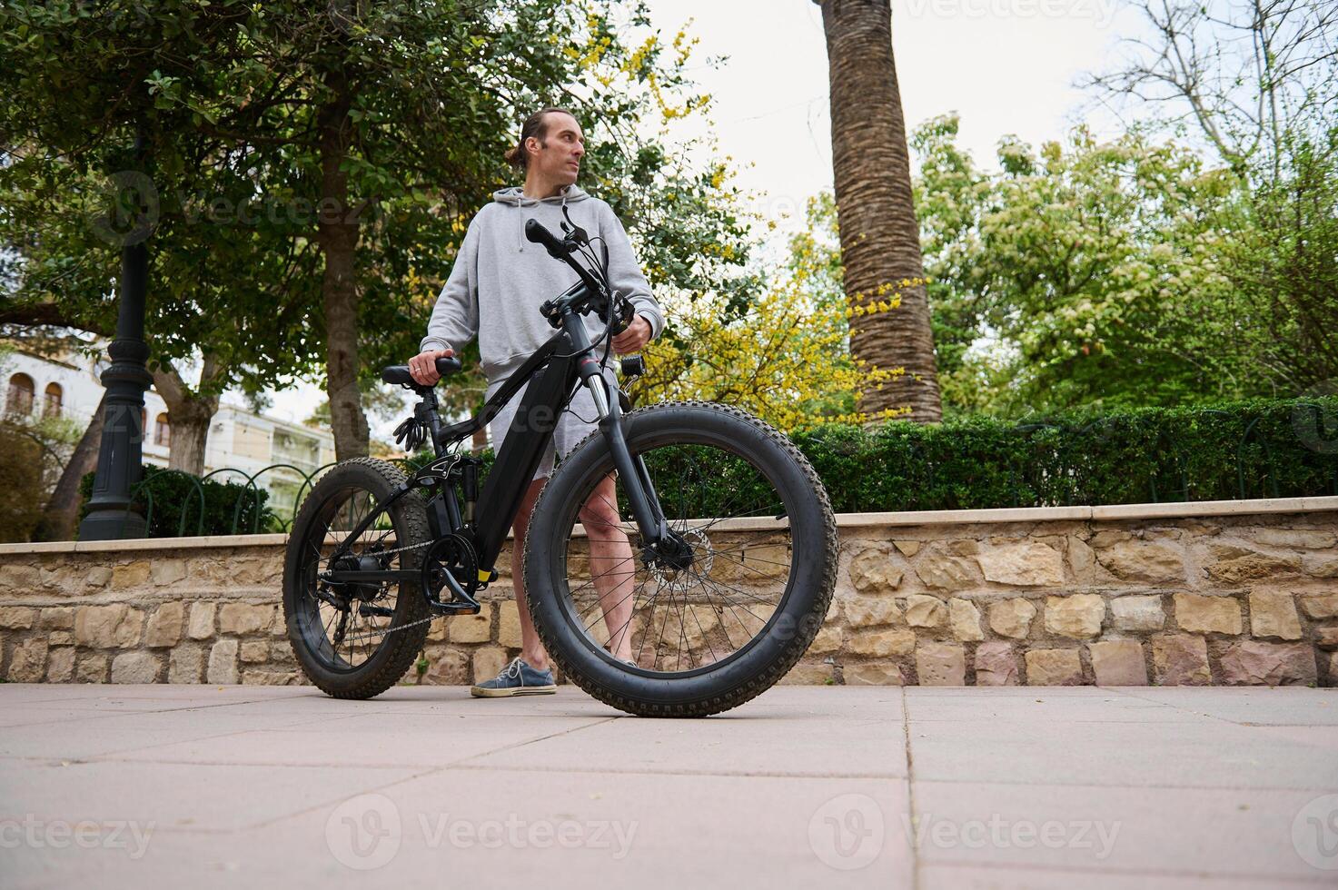 faible angle vue de homme dans gris sweat à capuche et des sports shorts, location un électrique bicyclette dans le ville. bicyclette partage ville un service photo