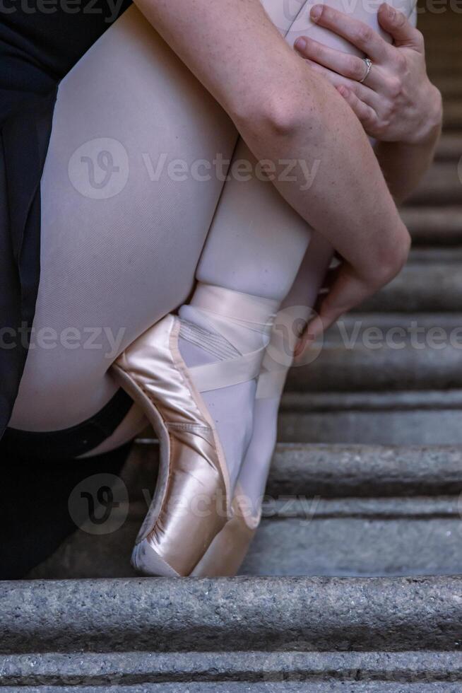 fermer de ballerine portant pointes des chaussures en portant sa mains sur sa chevilles tandis que séance sur le gris pierre pas. Danse repos sur le escalier. danseurs pieds avec rose ballet chaussons sur. copie espace photo