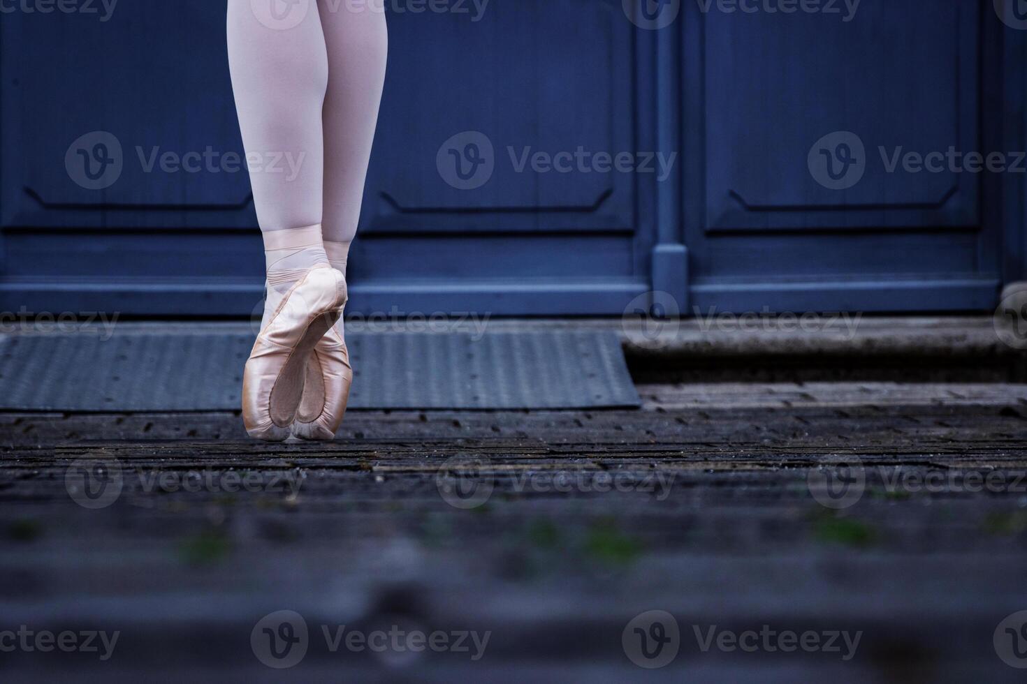 fermer de une Danseur jambes équilibrage sur le pointe chaussures. ballerine portant ballet chaussons tandis que permanent sur sa conseils sur le pavé route. gris rétro des portes sur le Contexte. sélectif concentrer photo