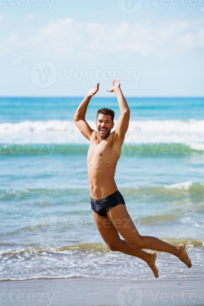 jeune homme avec un beau corps en maillot de bain sautant sur une plage tropicale. photo