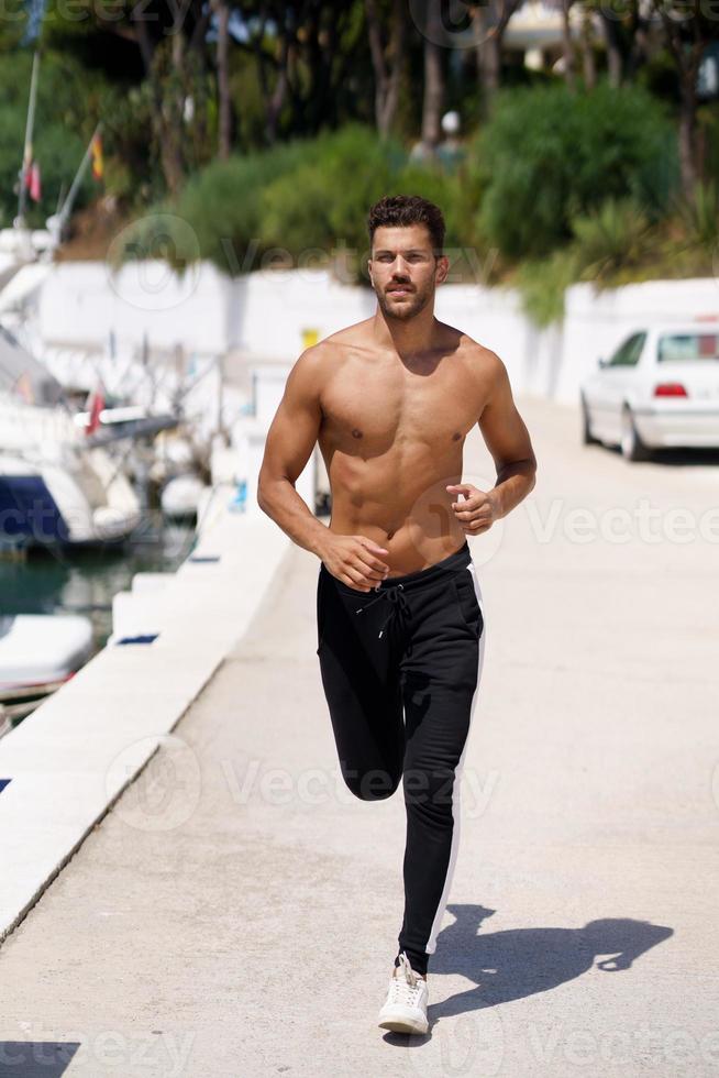 jeune homme au corps athlétique courant torse nu dans un port. photo