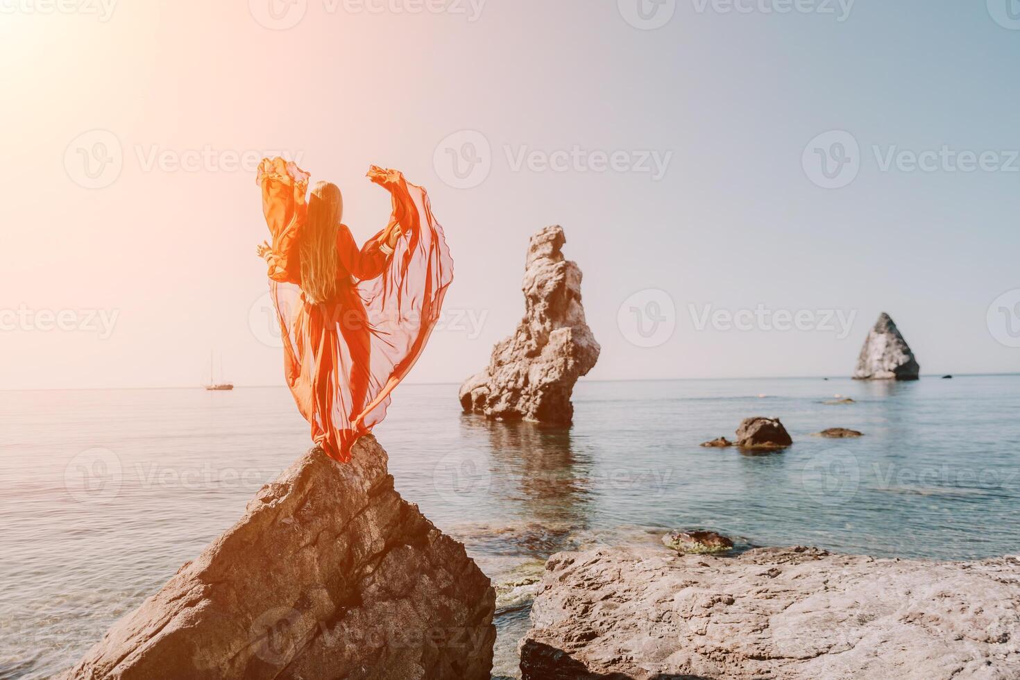 femme Voyage mer. Jeune content femme dans une longue rouge robe posant sur une plage près le mer sur Contexte de volcanique rochers, comme dans Islande, partage Voyage aventure périple photo