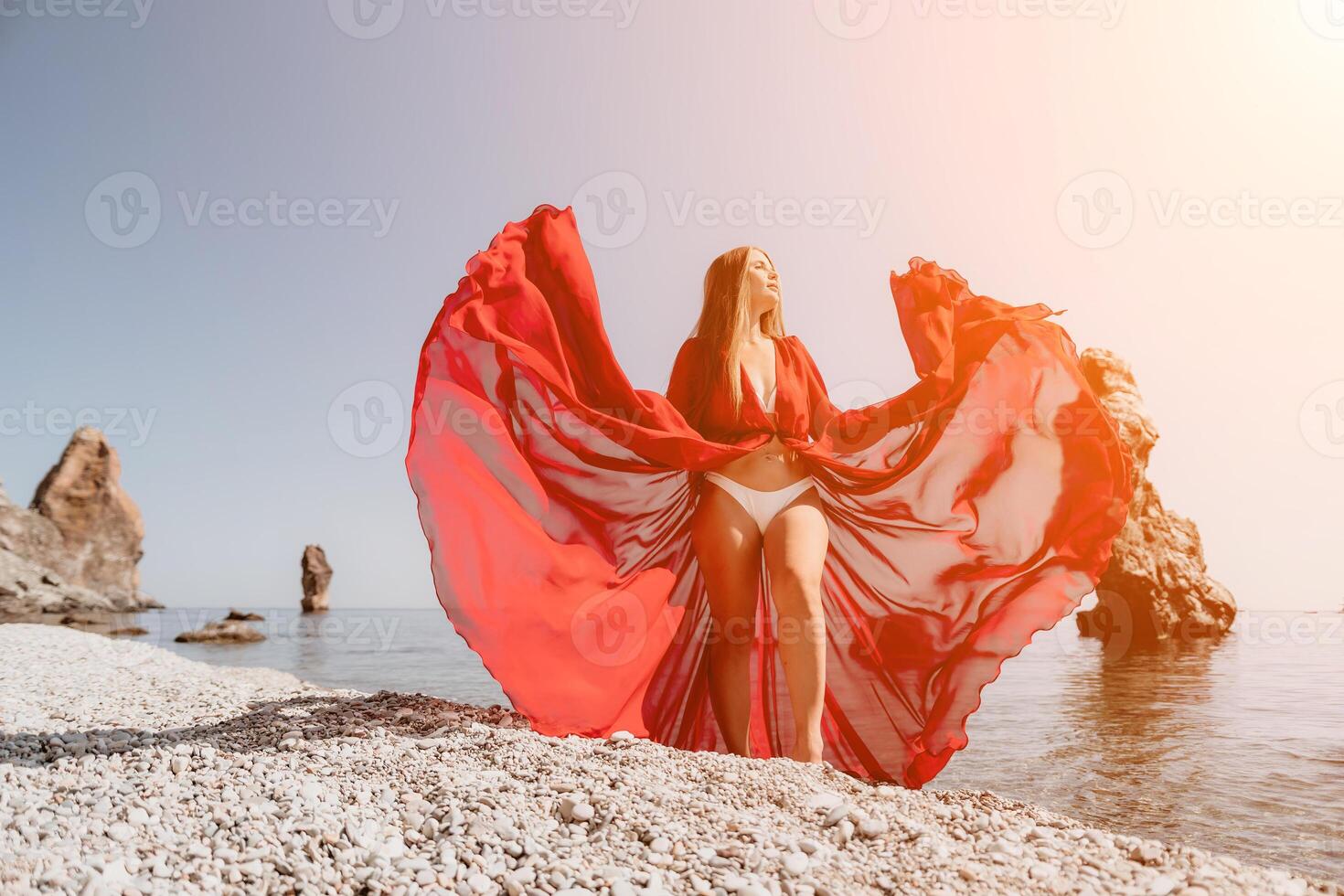 femme Voyage mer. content touristique dans rouge robe prendre plaisir prise image en plein air pour souvenirs. femme voyageur posant sur le Roche à mer baie entouré par volcanique montagnes, partage Voyage aventure périple photo