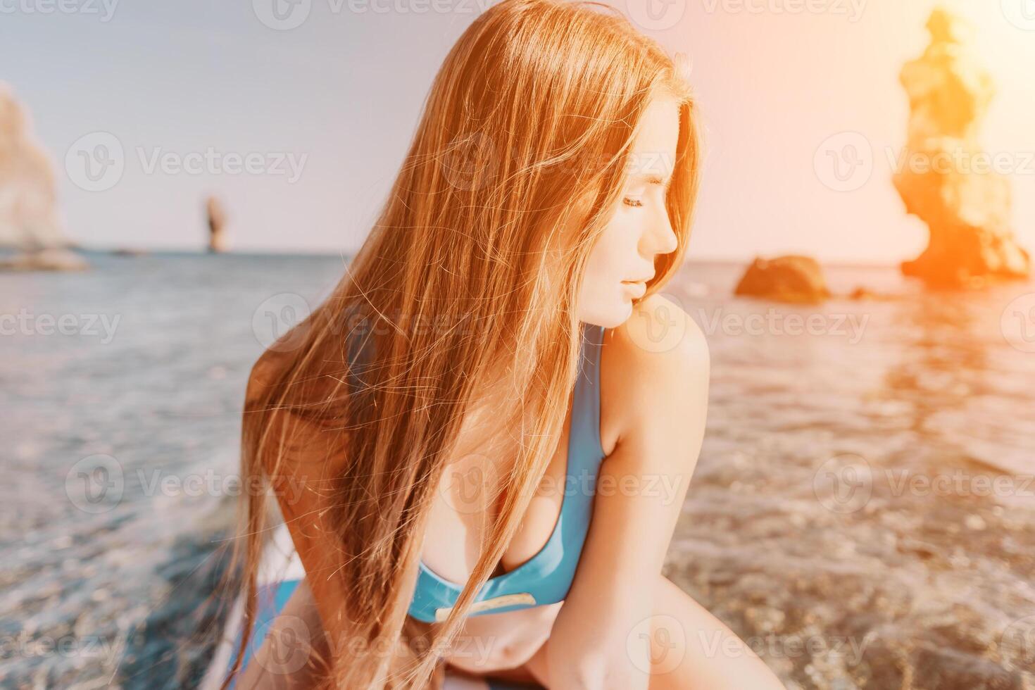 femme mer souper. proche en haut portrait de content Jeune caucasien femme avec longue cheveux à la recherche à caméra et souriant. mignonne femme portrait dans une bleu bikini posant sur souper planche dans le mer photo