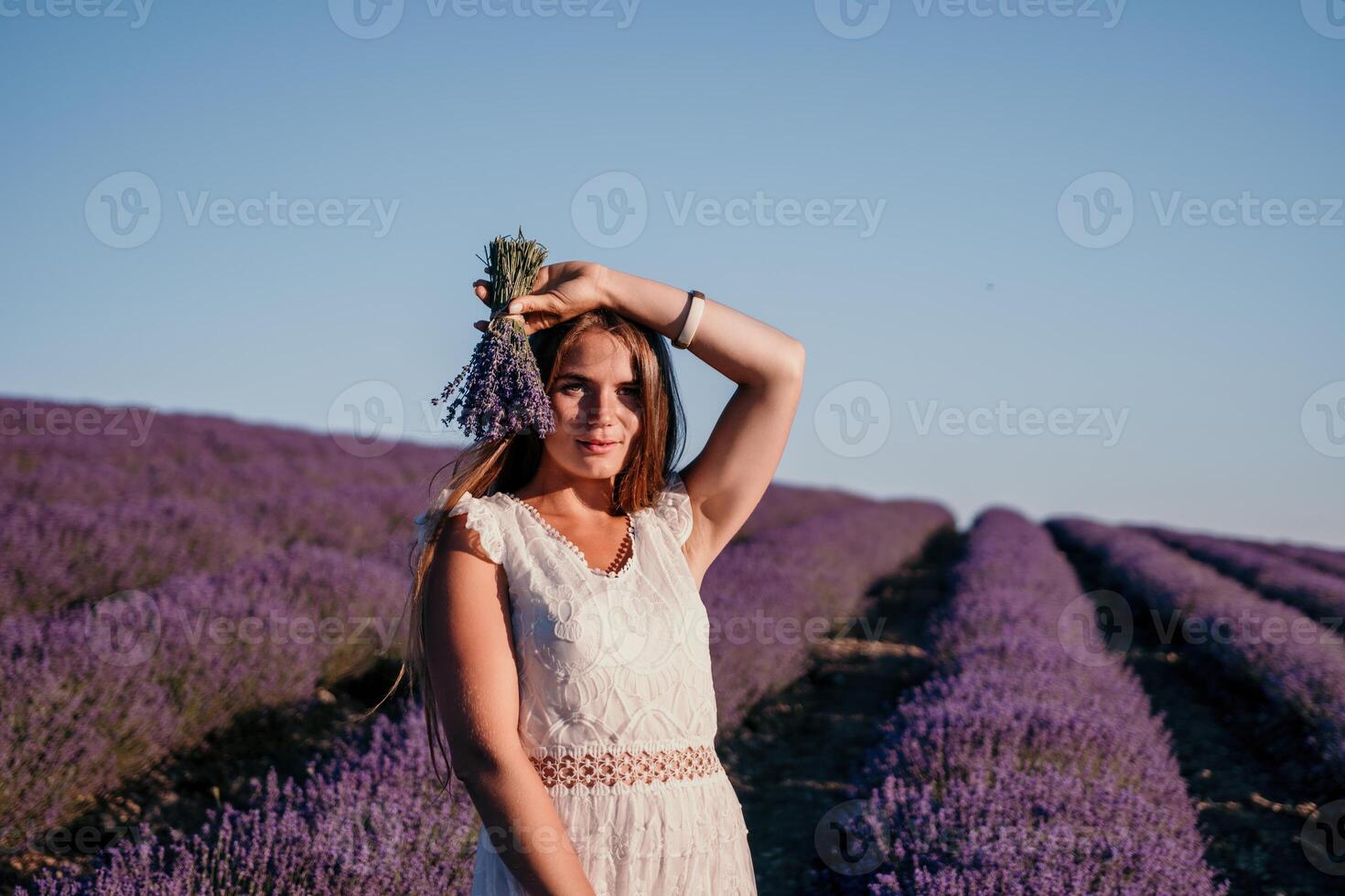 femme lavande champ. content insouciant femme dans une blanc robe en marchant dans une lavande champ et odeur une lavande bouquet sur le coucher du soleil. idéal pour chaud et inspirant concepts dans esprit d'aventure et Voyage. photo