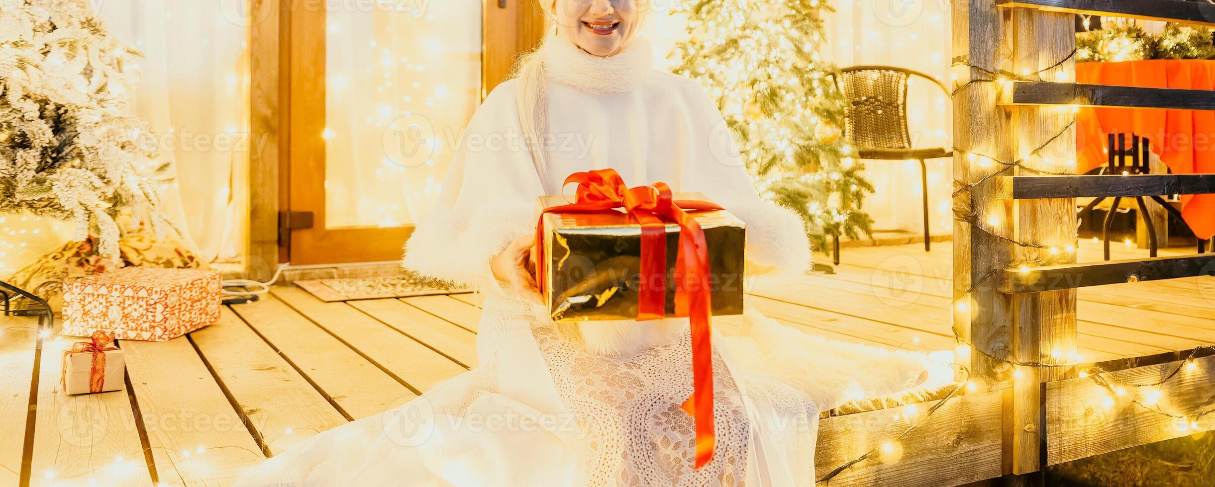 content souriant femme dans une blanc robe en portant une cadeau boîte dans de face de une Noël arbre. photo