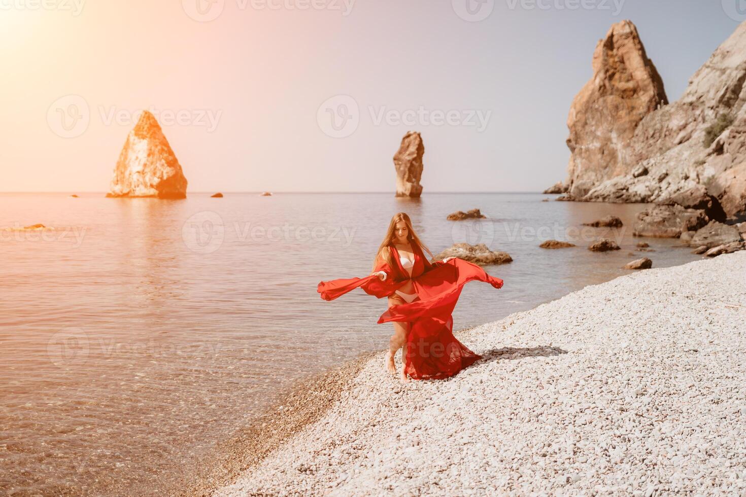 femme Voyage mer. content touristique dans rouge robe prendre plaisir prise image en plein air pour souvenirs. femme voyageur posant sur le Roche à mer baie entouré par volcanique montagnes, partage Voyage aventure périple photo