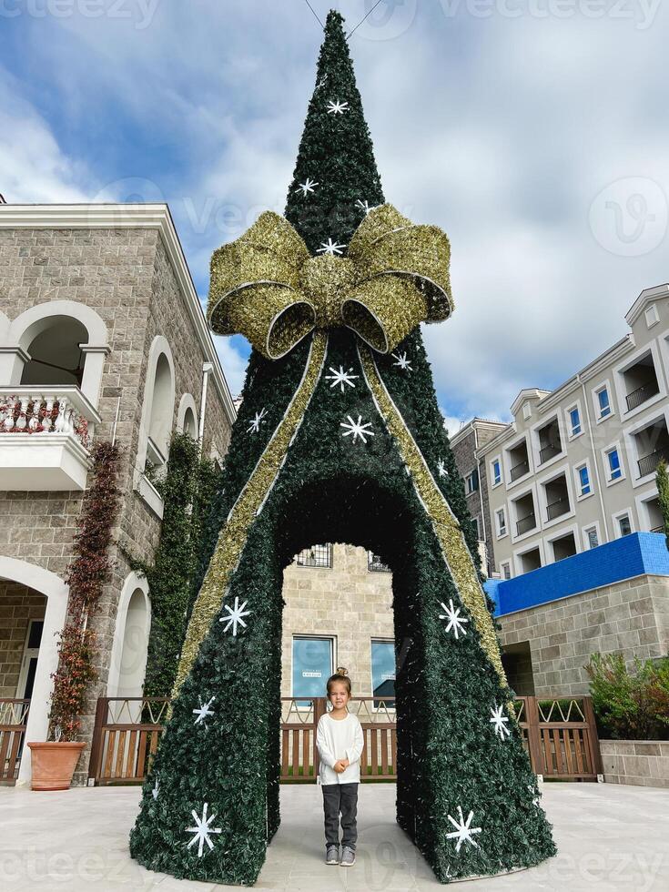 peu fille des stands près le Noël arbre avec un cambre et une arc photo