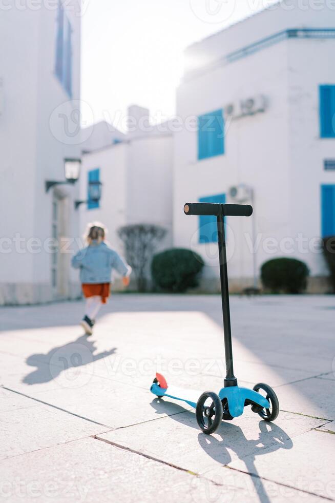 scooter des stands sur une tuile dans le Cour de le maison contre le Contexte de une peu fille en marchant vers l'avant photo