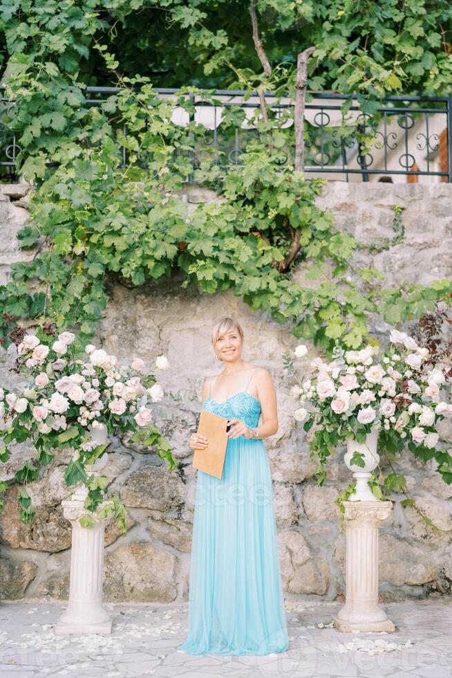 femelle réceptionniste avec une enregistrement livre des stands près une fleur demi-arc contre une mur dans le jardin photo