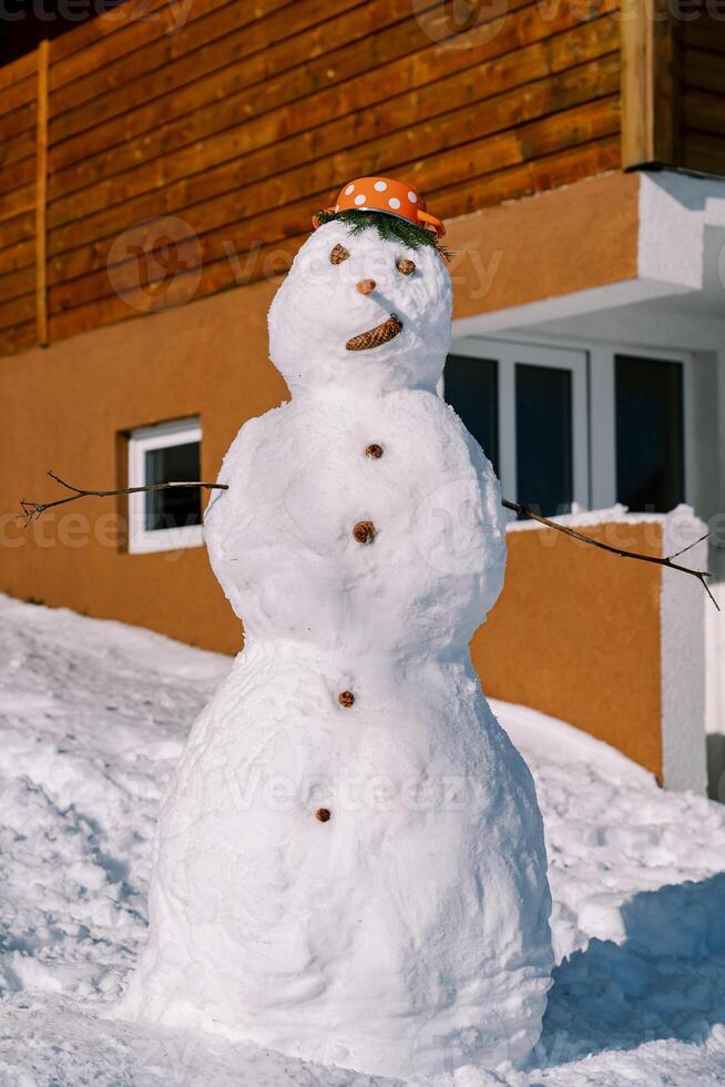 bonhomme de neige avec une casserole avec rouge polka points sur le sien tête des stands près une en bois maison photo