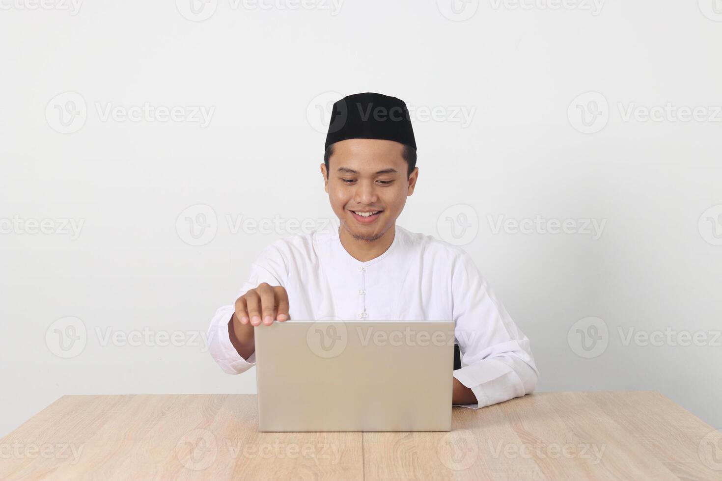 portrait de excité asiatique musulman homme dans koko chemise avec calotte travail sur le sien portable pendant jeûne sur Ramadan mois. isolé image sur blanc Contexte photo