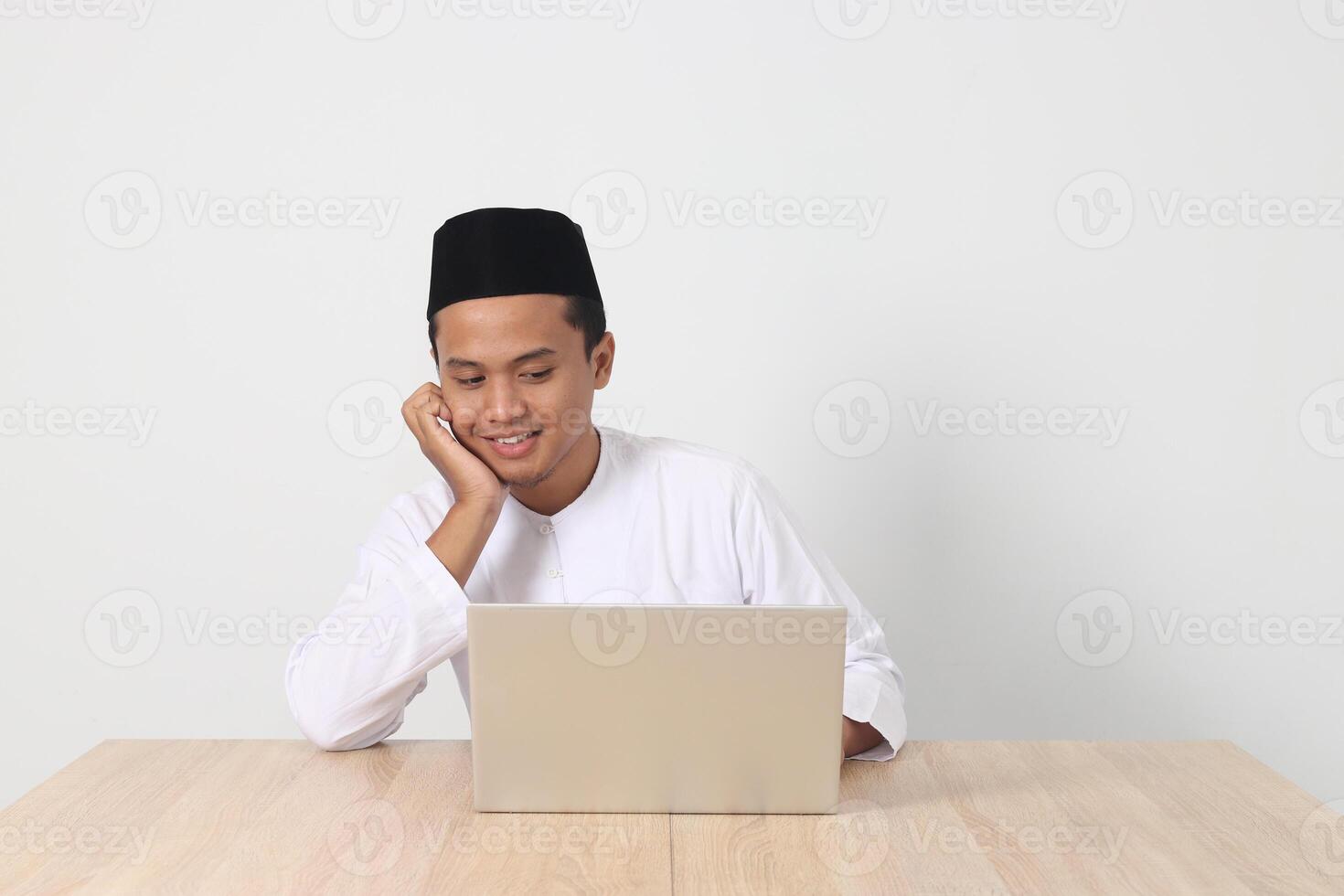 portrait de excité asiatique musulman homme dans koko chemise avec calotte travail sur le sien portable pendant jeûne sur Ramadan mois. isolé image sur blanc Contexte photo