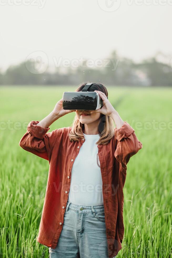 femme dans une décontractée tenue des stands dans une luxuriant vert champ, explorant virtuel environnements avec une virtuel réalité casque. photo