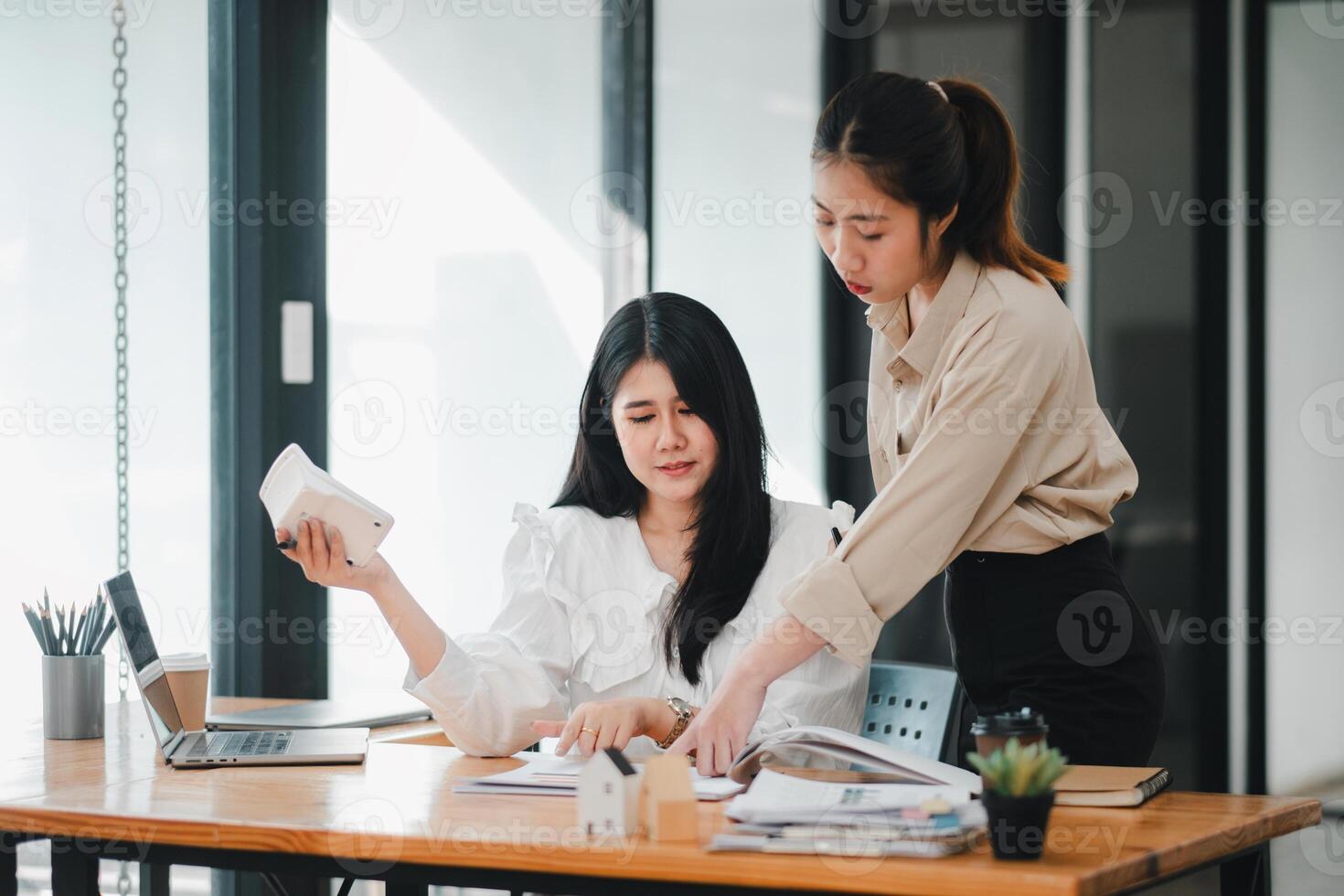 deux femelle réel biens professionnels discuter projet détails avec une modèle maison sur le tableau, symbolisant projet Planification et travail en équipe. photo