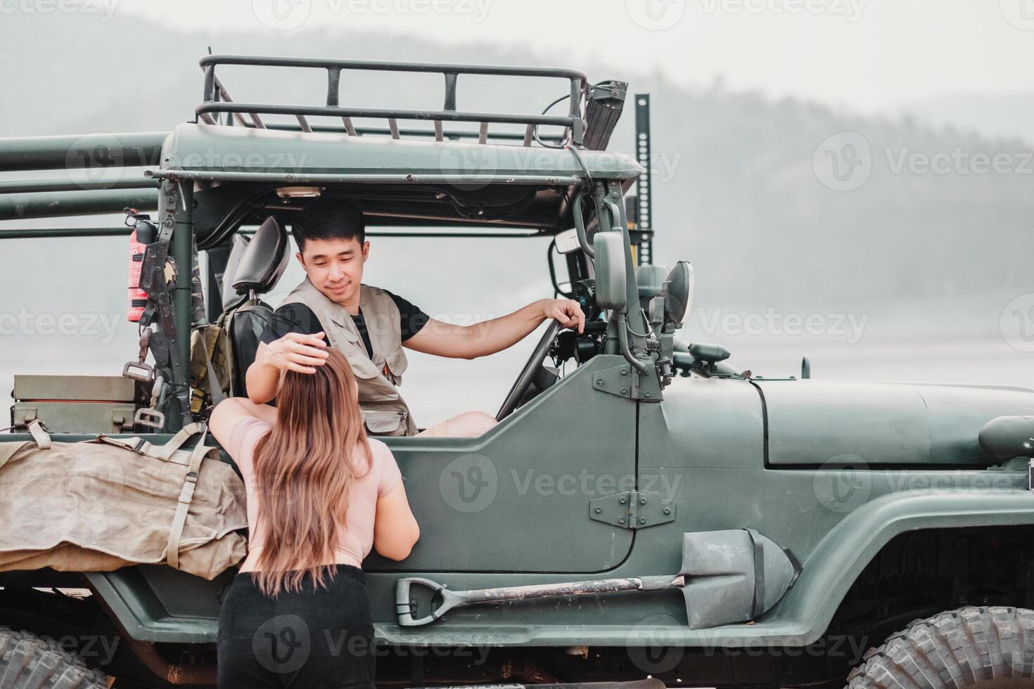 soins homme assiste une femme comme elle grimpe dans une solide hors route voiture pour un aventure par une brumeux Lac à aube. photo