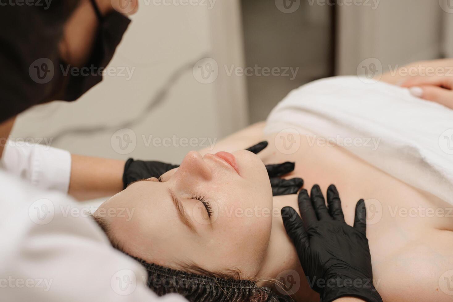 fermer de une qualifié massothérapeute femme mains masser femelle client faciale peau. beauté traitement concept photo