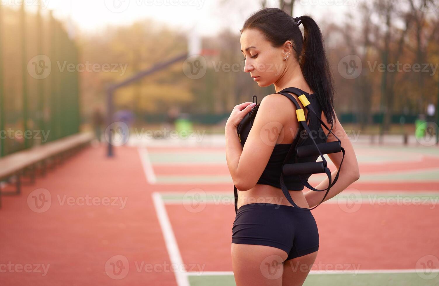 fille athlète formation en utilisant trx sur terrain de sport. mixte course Jeune adulte femme faire faire des exercices avec suspension système. en bonne santé mode de vie. élongation en plein air Cour de récréation. photo