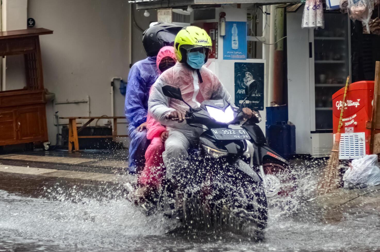 une mère, père et enfant comme une famille balade une moto portant imperméables par les eaux de crue pendant lourd pluie dans une Résidentiel zone, Indonésie, 8 décembre 2023. photo