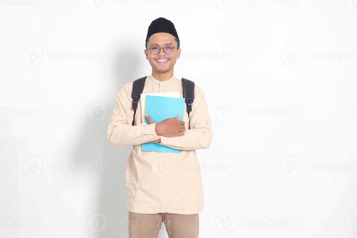 portrait de excité étudiant asiatique musulman homme dans koko chemise avec calotte porter sac à dos, tandis que en portant le sien école livres. islamique éducation concept. isolé image sur blanc Contexte photo