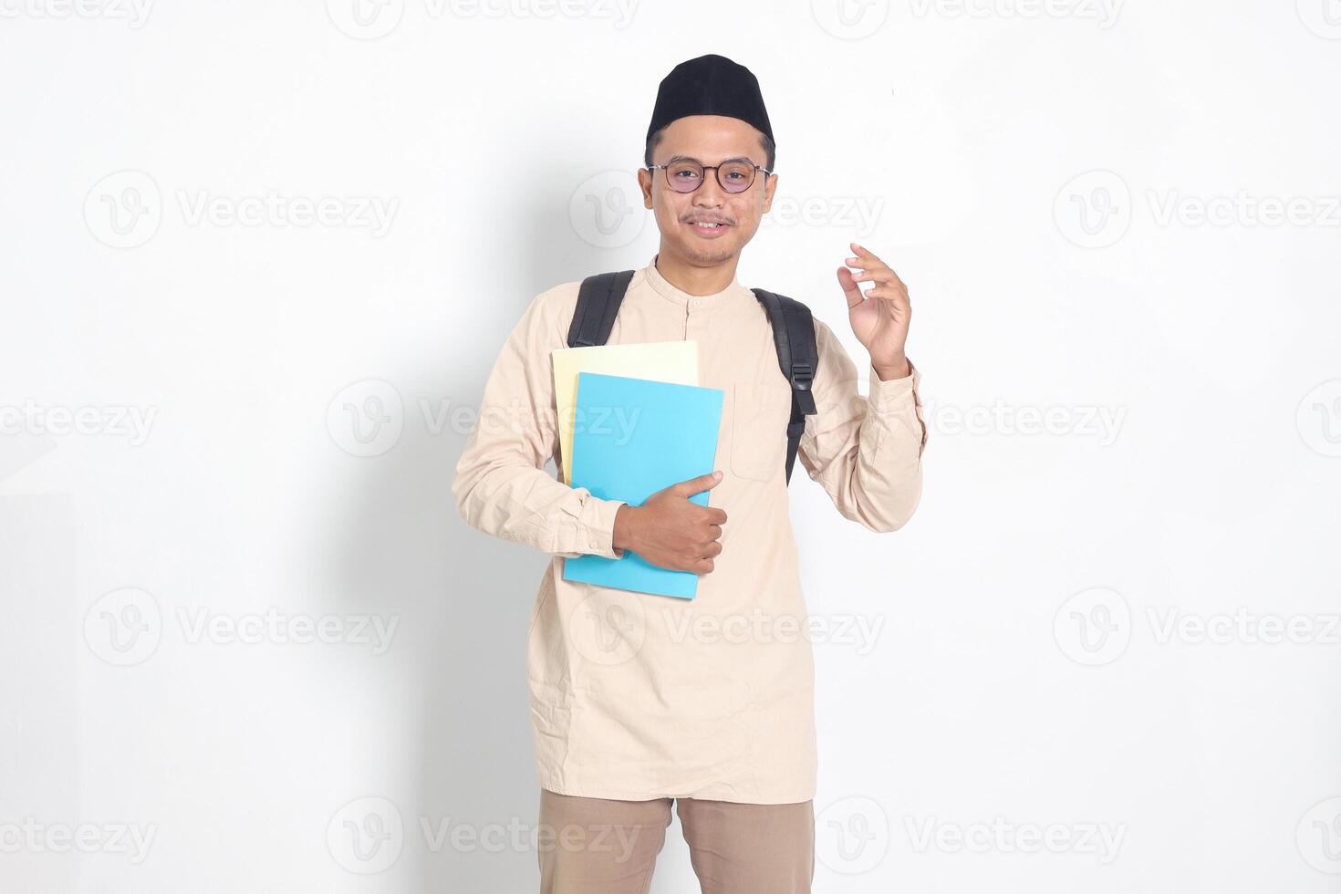 portrait de excité étudiant asiatique musulman homme dans koko chemise avec calotte porter sac à dos, tandis que en portant le sien école livres. islamique éducation concept. isolé image sur blanc Contexte photo