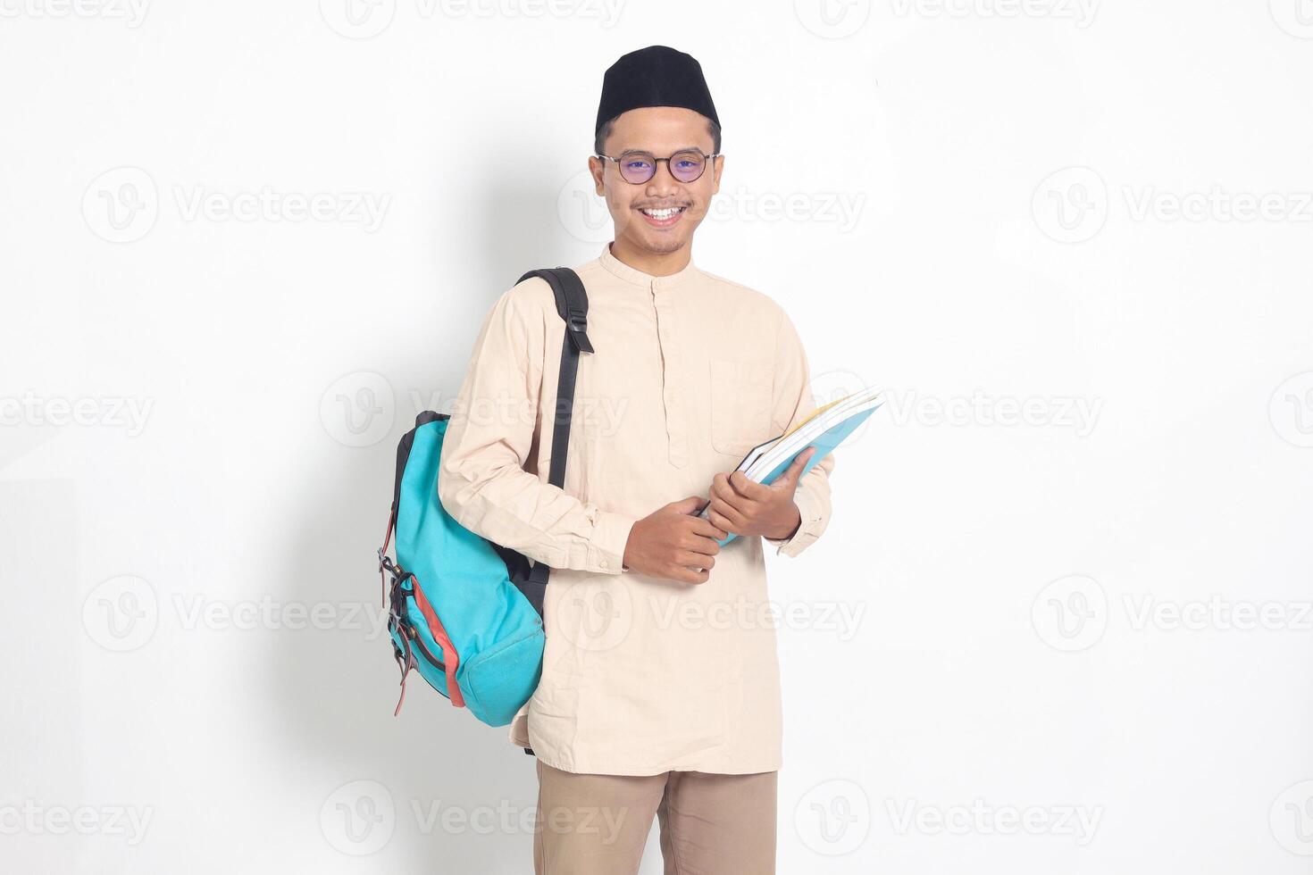 portrait de excité étudiant asiatique musulman homme dans koko chemise avec calotte porter sac à dos, tandis que en portant le sien école livres. islamique éducation concept. isolé image sur blanc Contexte photo