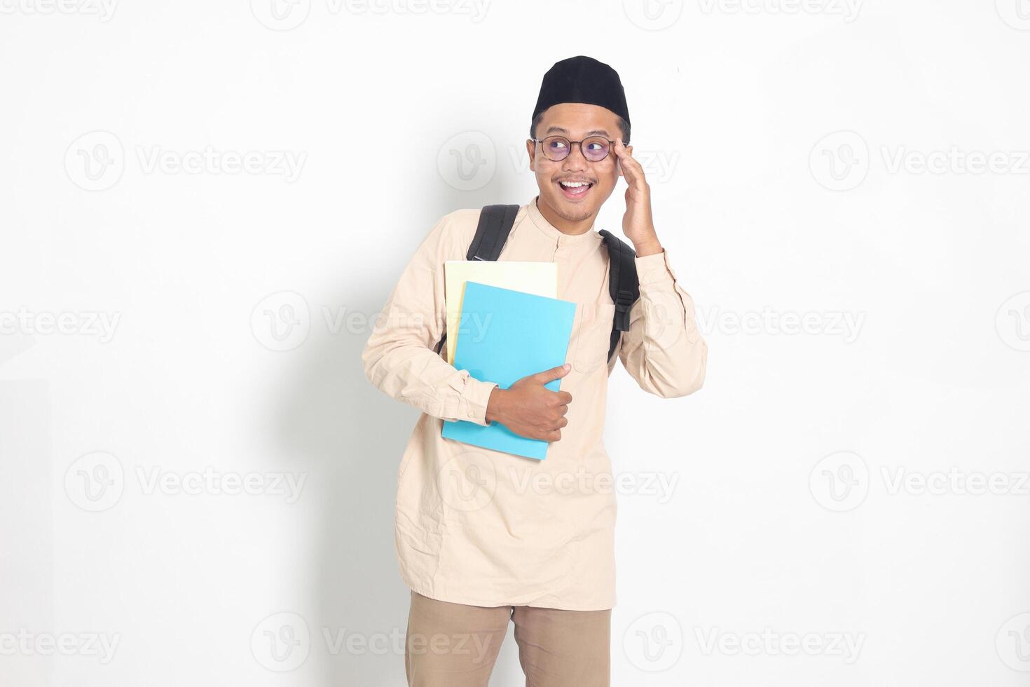 portrait de excité étudiant asiatique musulman homme dans koko chemise avec calotte porter sac à dos, tandis que en portant le sien école livres. islamique éducation concept. isolé image sur blanc Contexte photo