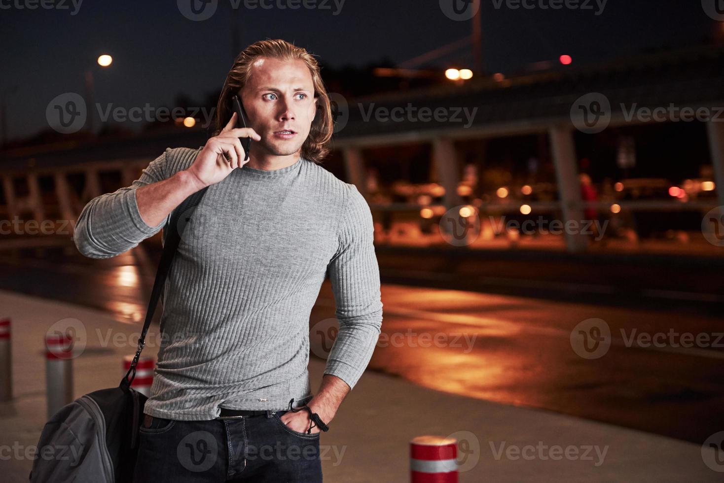 regard tendu. jeune homme élégant marchant dans la rue nocturne près de la route et ayant une conversation au téléphone photo